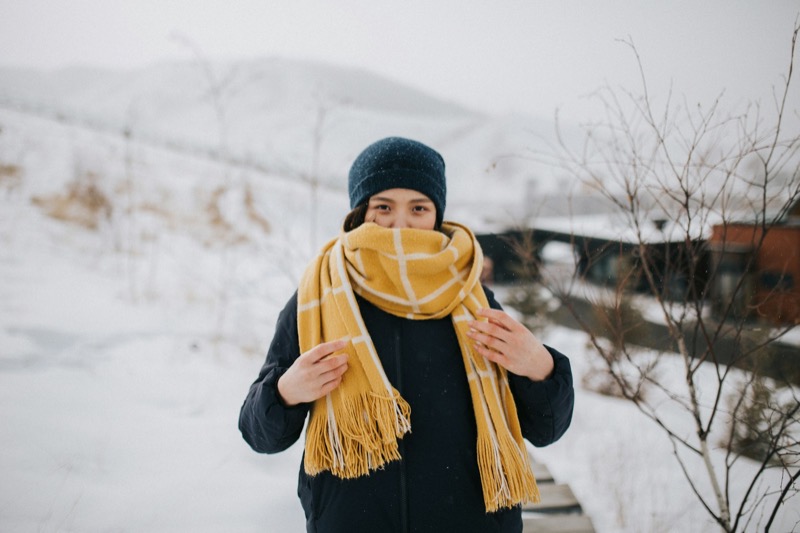 Person i mörk rock med saffransgul frans-sjal, snölandskap bakom